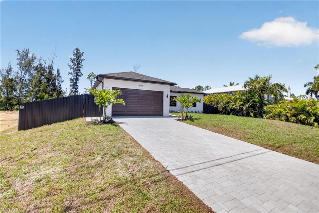 Contemporary single-story residence featuring a two-car garage with a wood-finish door, a light-colored stucco exterior, and a dark shingle roof