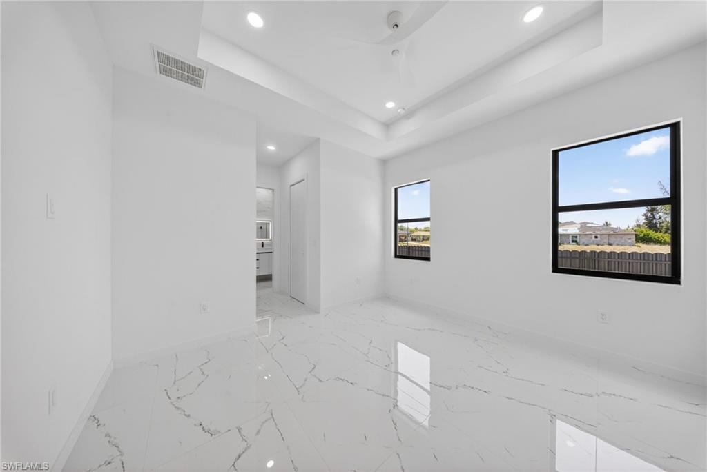 Spacious room featuring large format marble-look tile flooring, two windows with black frames, a tray ceiling, and recessed lighting