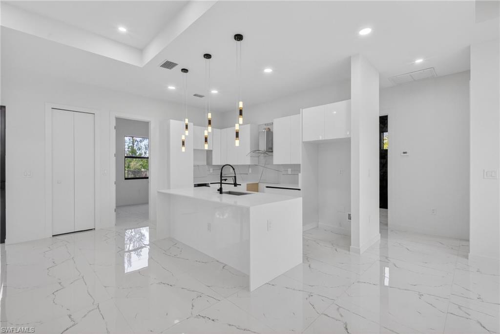 Kitchen featuring a white waterfall island, pendant lighting, white cabinetry, and a black faucet