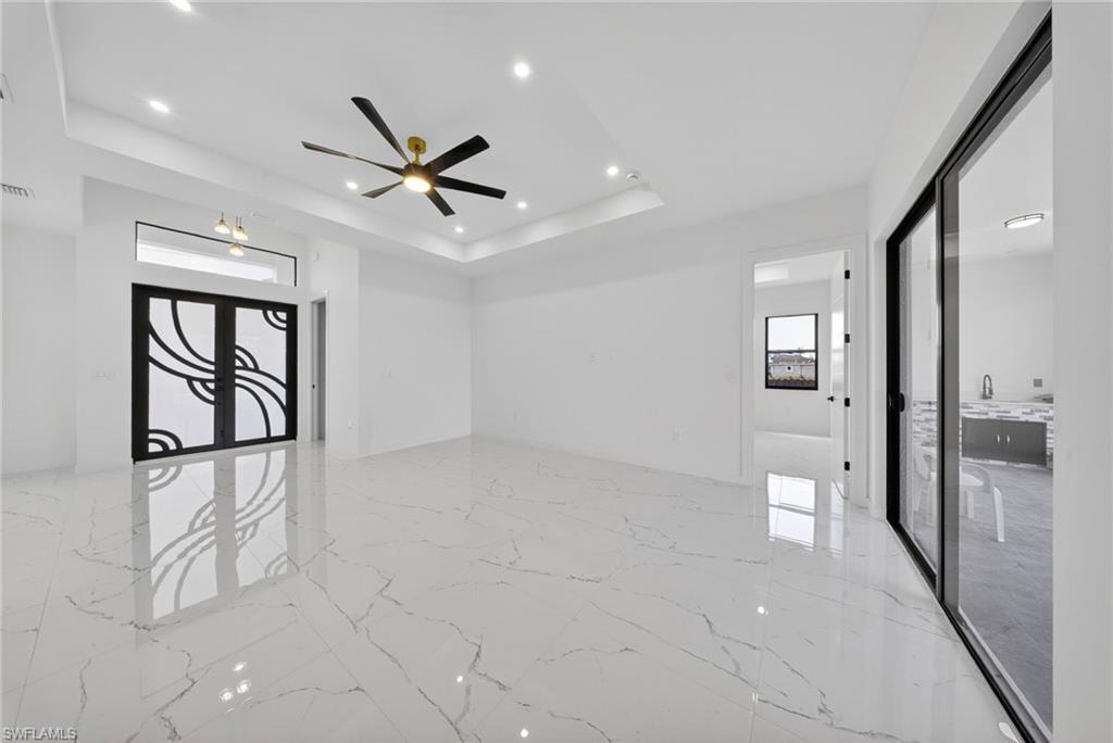 Spacious interior featuring marble-look tile flooring, a tray ceiling with recessed lighting, and a modern ceiling fan