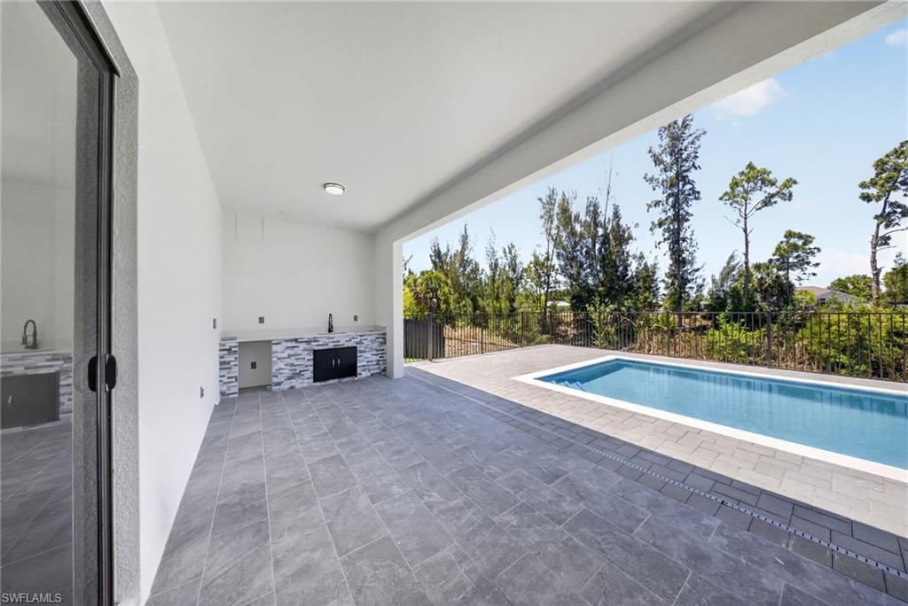 Covered outdoor living space featuring an integrated outdoor kitchen with stone veneer accents and a built-in grill
