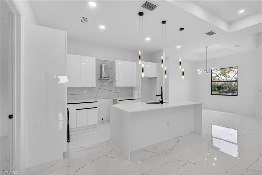 Modern kitchen featuring glossy white cabinetry, a spacious island with an integrated sink and black faucet, and contemporary pendant lighting
