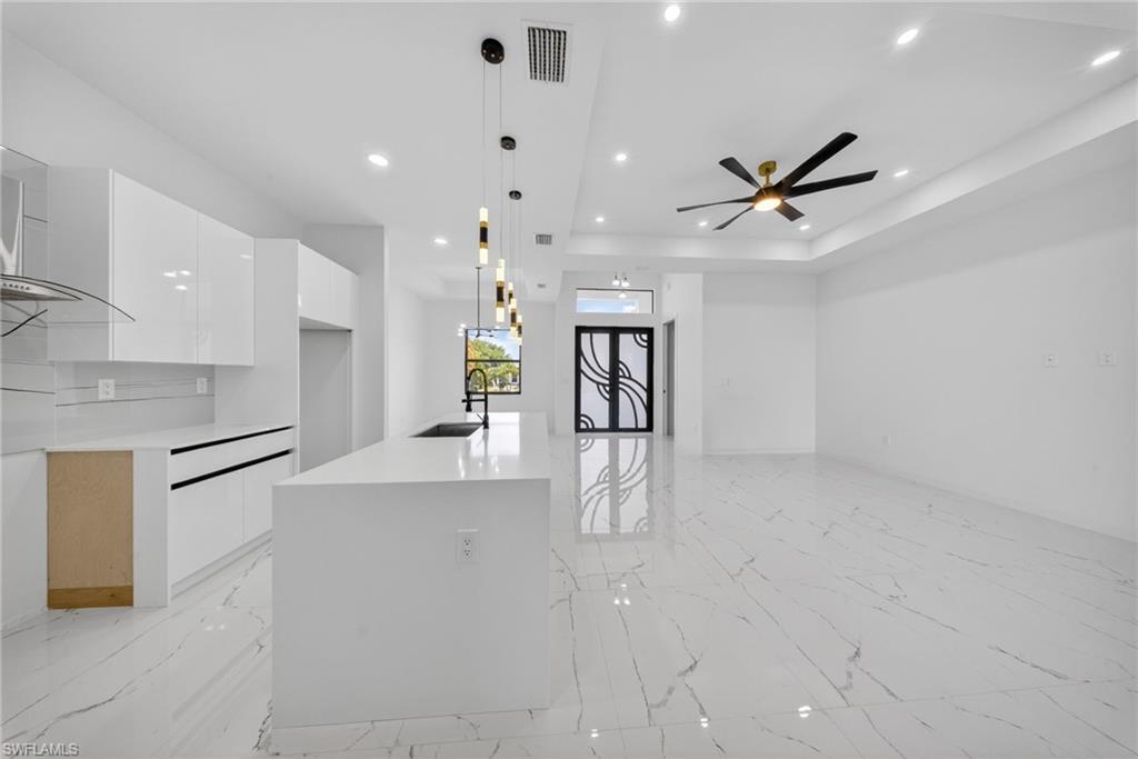 Open concept interior featuring large format marble-look tile flooring, a modern kitchen island with an undermount sink, recessed lighting, a contemporary ceiling fan, and an architectural front door