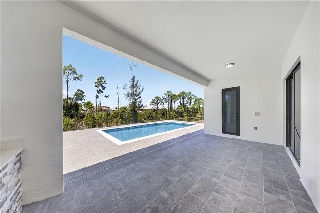 Expansive covered patio featuring large format tile flooring, a built-in outdoor counter with stacked stone detailing, and direct access to the rectangular swimming pool
