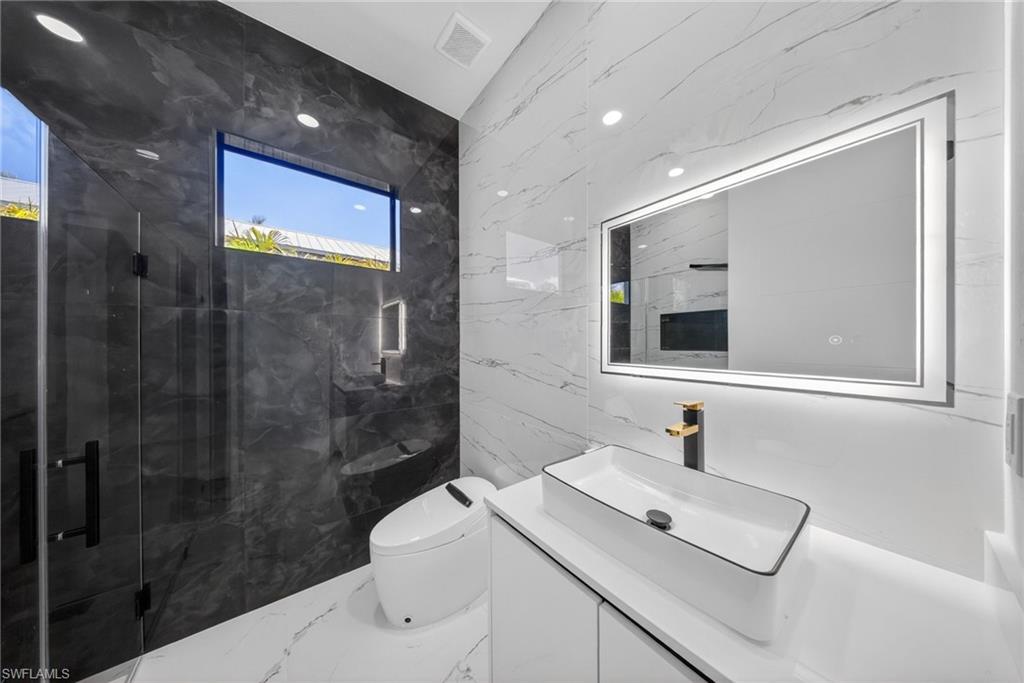 Modern bathroom featuring a rectangular vessel sink with a black and gold-tone faucet, a backlit vanity mirror, and recessed lighting
