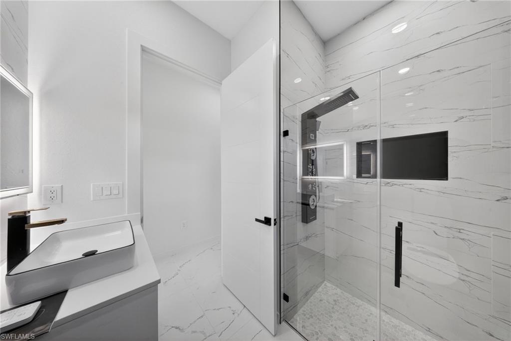 Contemporary bathroom with a frameless glass shower enclosure, a multi-function shower panel, and white marble-look wall and floor tiling