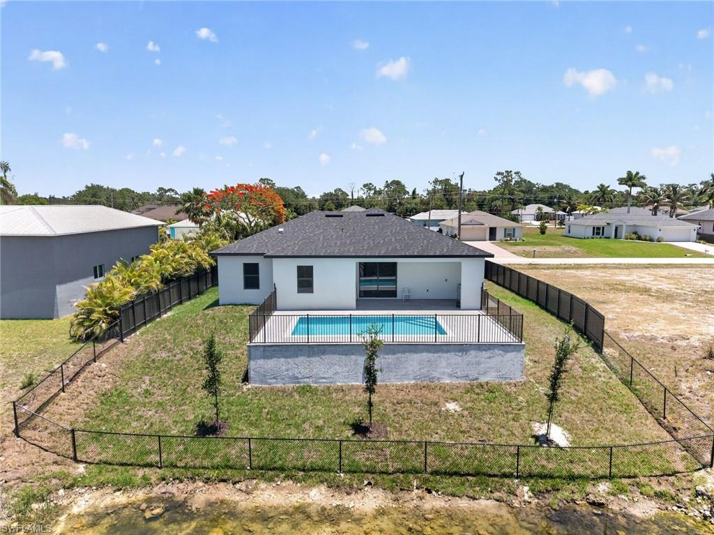Rear elevation featuring a private swimming pool with a black aluminum fence surround, a covered patio, and a dark shingle roof