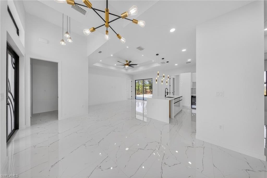 Spacious interior featuring high vaulted ceilings, large format white tile flooring with veining, and a modern kitchen island with pendant lighting