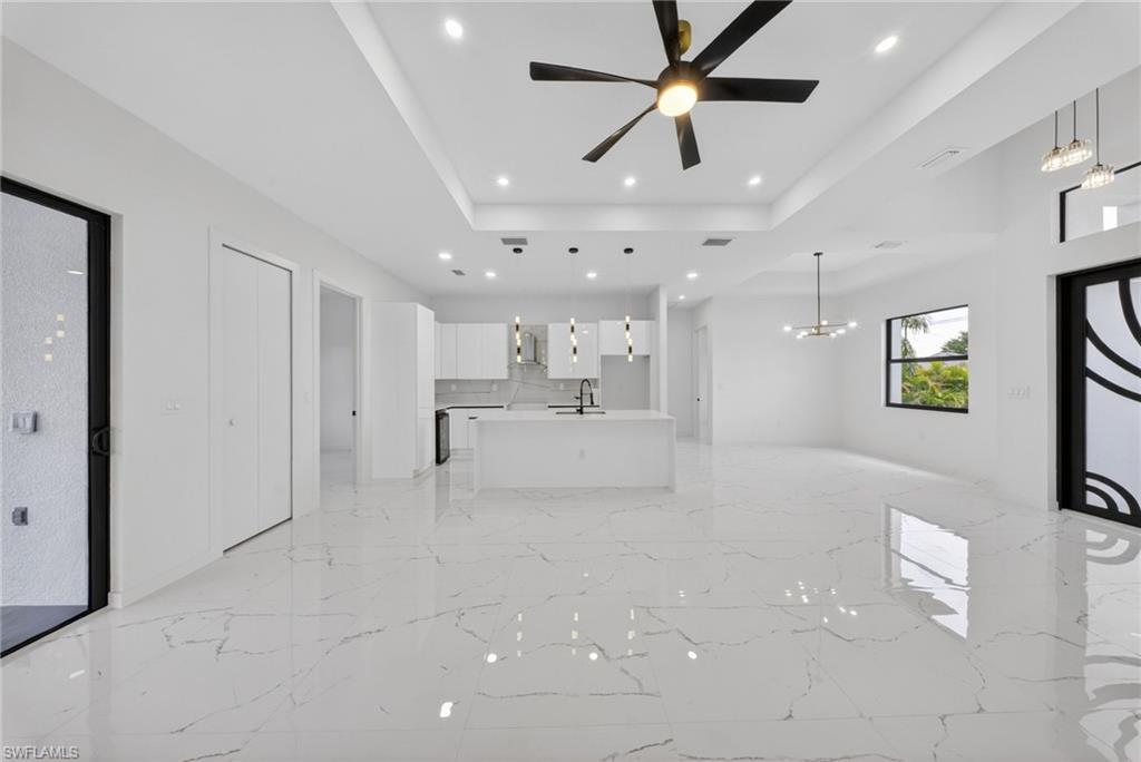 Open-concept living space featuring sleek white cabinetry, a kitchen island with sink, and white countertops