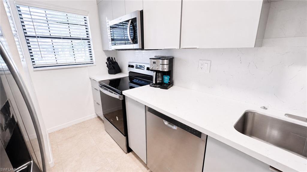 Contemporary kitchen featuring white cabinetry, stainless steel appliances, a white tile backsplash, a stainless steel sink, and light-colored flooring