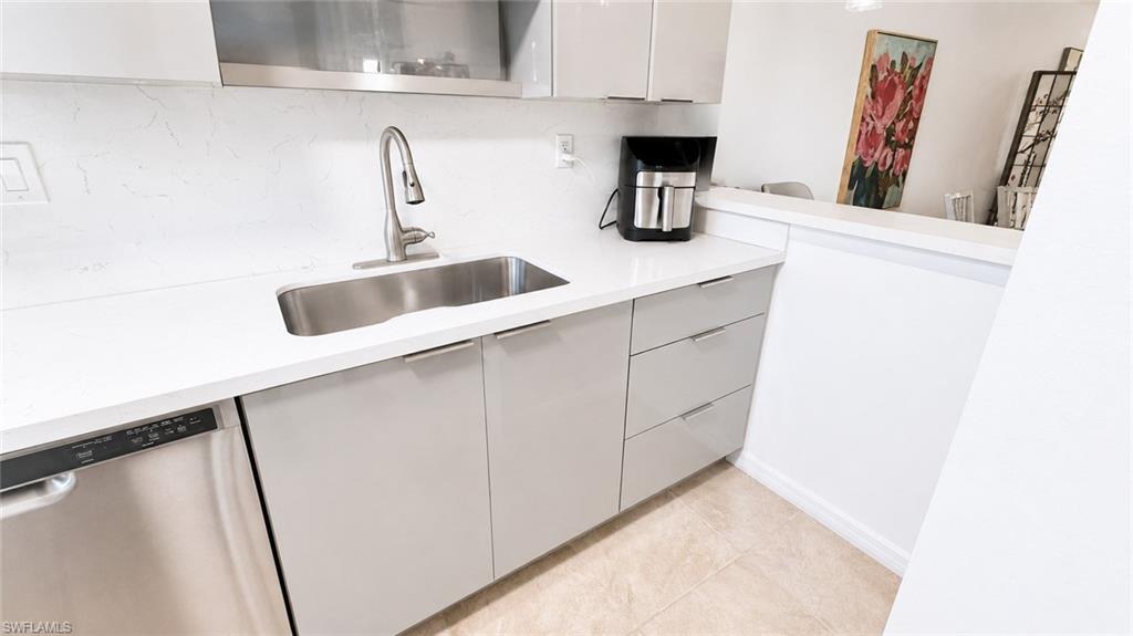 Kitchen featuring a stainless steel undermount sink with a gooseneck faucet, light-toned countertops, contemporary cabinetry with flat-panel doors and drawer fronts, and a built-in stainless steel dishwasher