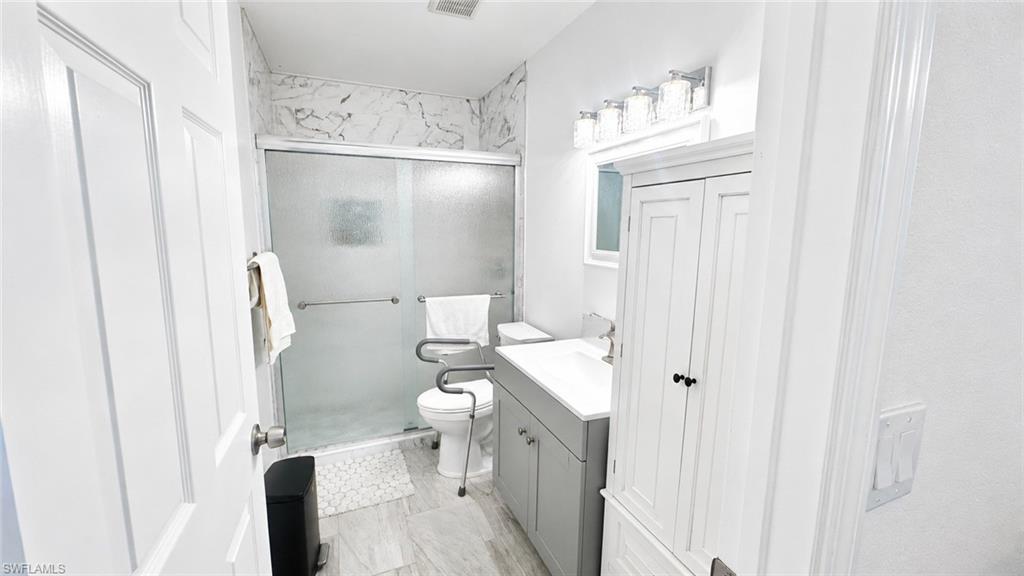 Bathroom featuring a sliding glass shower enclosure with marbled wall tile, a gray vanity with an integrated sink, a mirrored medicine cabinet, and overhead vanity lighting