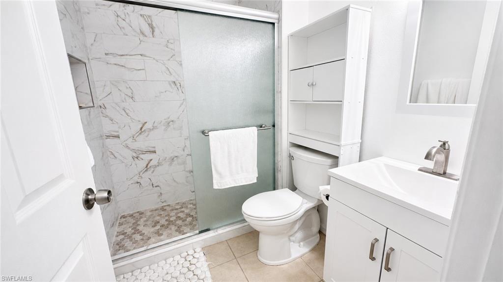 Bathroom featuring a glass-enclosed shower with large format marble-look tile, a mosaic tile shower floor, and a built-in shower niche