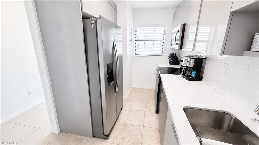Updated kitchen featuring stainless steel appliances, white countertops, a single basin sink, and glossy white cabinetry