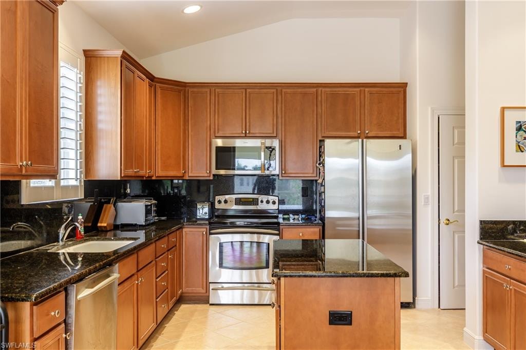 Kitchen featuring sink, stainless steel appliances, a kitchen island, vaulted ceiling, and dark stone counters