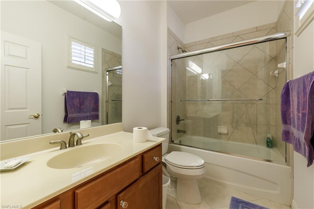 Full bathroom featuring vanity, bath / shower combo with glass door, tile patterned floors, and toilet