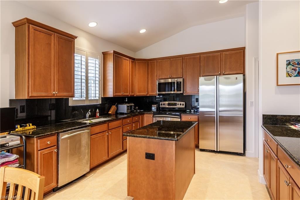 Kitchen featuring a kitchen island, appliances with stainless steel finishes, dark stone countertops, and lofted ceiling