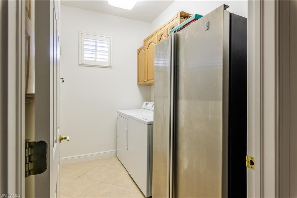 Washroom with light tile patterned flooring, cabinets, and washing machine and dryer