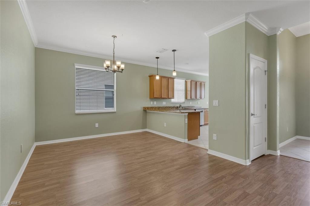 Kitchen featuring a peninsula, light stone counters, light wood-type flooring, crown molding, and hanging lights