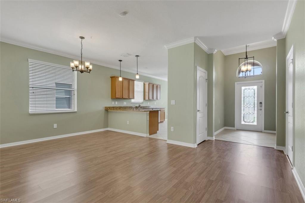 Foyer entrance with suspended lighting, ornamental molding, plenty of natural light, and wood finished floors