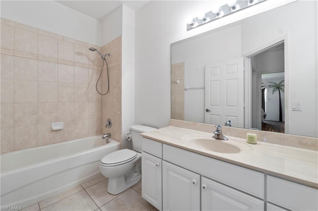 Bathroom featuring a full-sized bathtub with tiled surround, a white toilet, and a vanity with a light-toned countertop and integrated sink