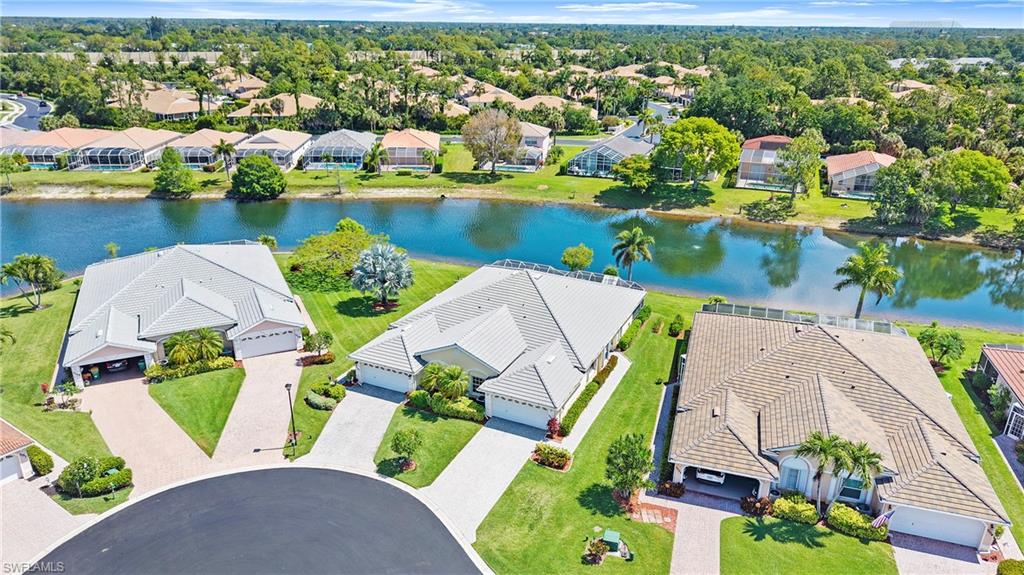 Waterfront property featuring a tile roof, mature palm trees, manicured lawns, and a paved driveway leading to an attached garage