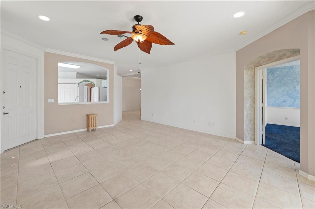 Spacious interior featuring neutral ceramic tile flooring, a decorative ceiling fan, recessed lighting, crown molding, and an arched entryway