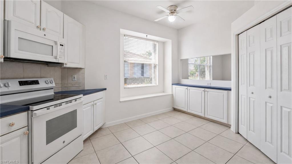 Kitchen area featuring white cabinetry, a built-in microwave, a white electric range, blue countertops, and neutral-toned tile flooring