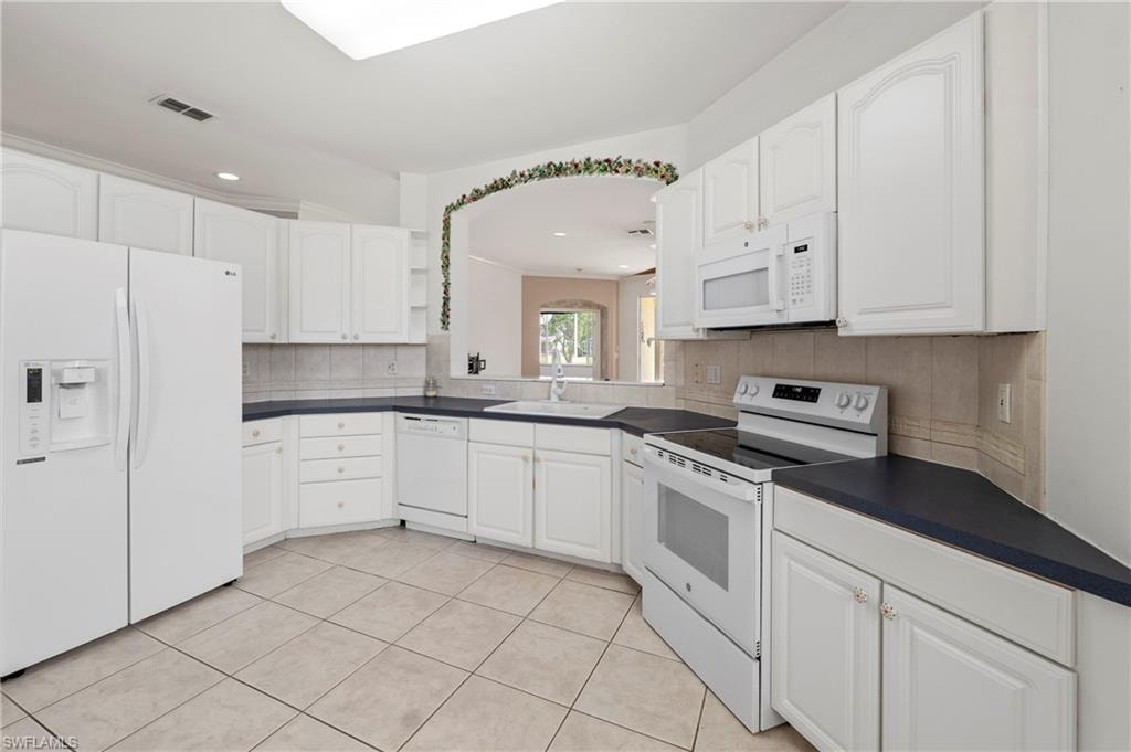 Spacious kitchen featuring white cabinetry, dark countertops, a built-in microwave, a full-size refrigerator, and tile flooring
