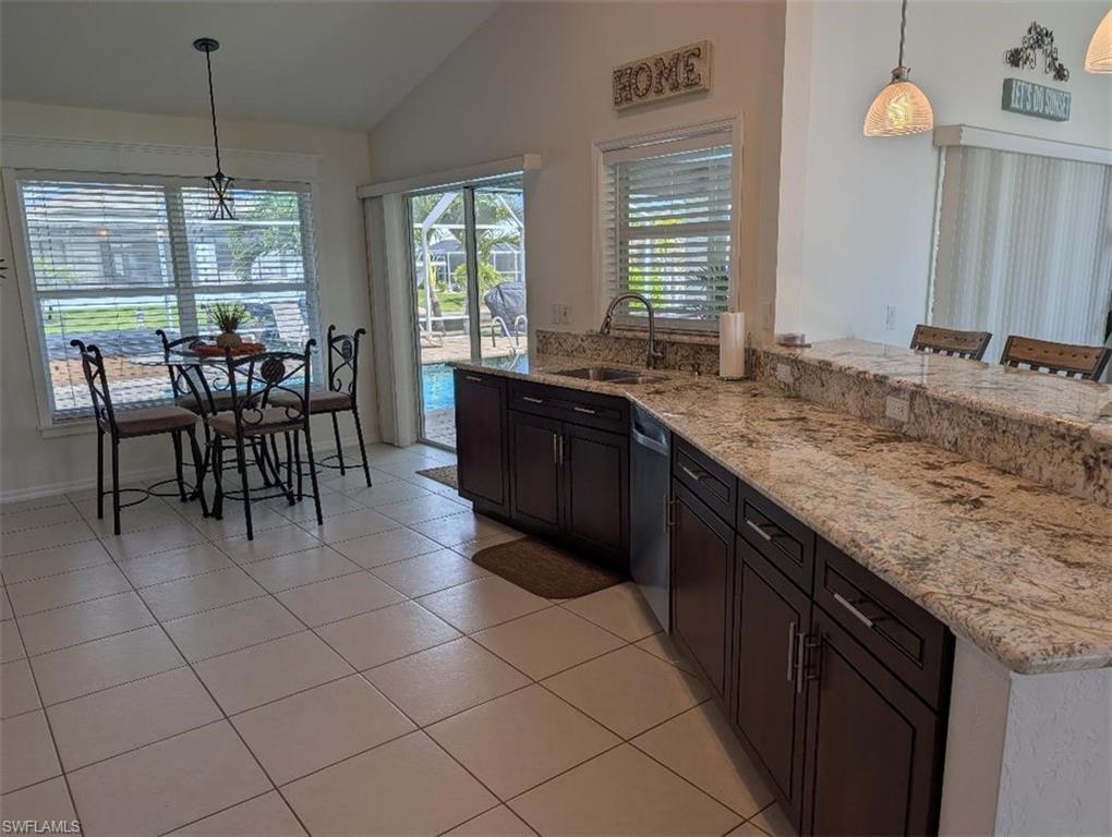 Kitchen with a sink, dishwasher, lofted ceiling, light stone counters, and pendant lighting