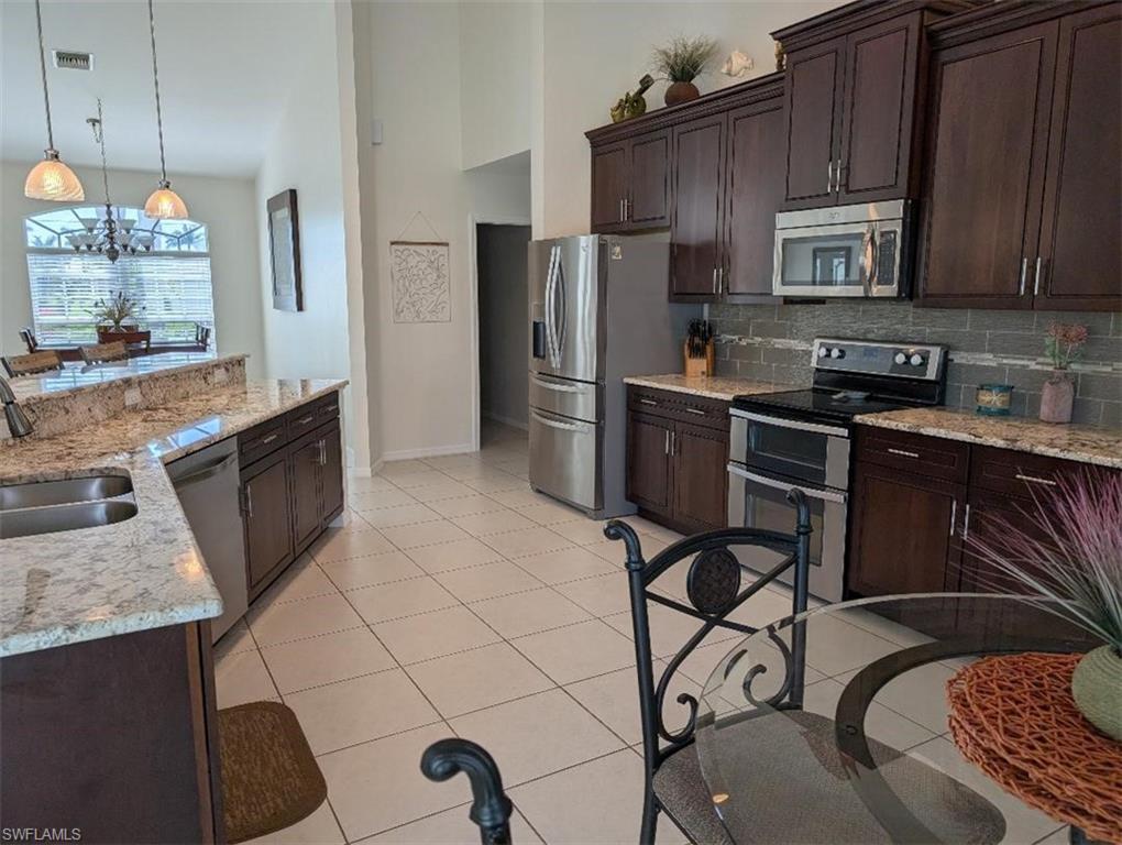 Kitchen featuring stainless steel appliances, a sink, baseboards, tasteful backsplash, and dark brown cabinets