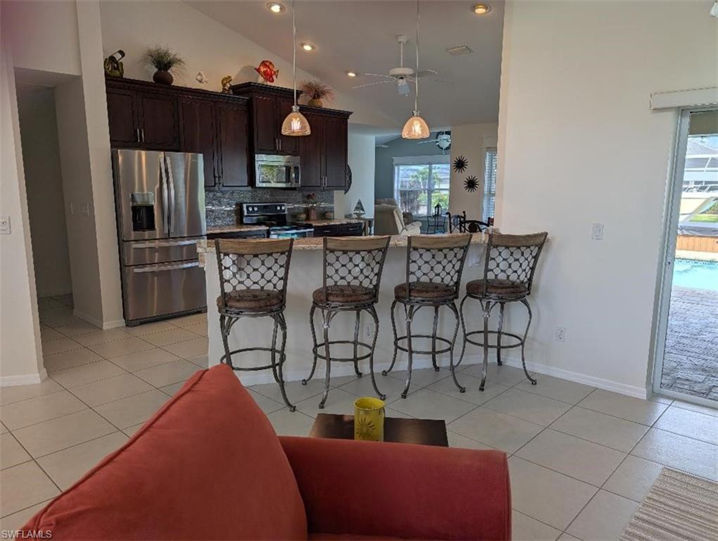Kitchen featuring stainless steel appliances, a kitchen breakfast bar, decorative backsplash, a ceiling fan, and dark brown cabinets