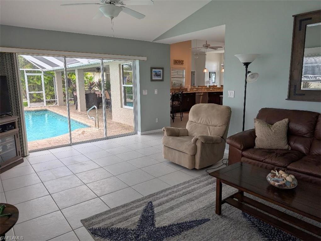 Living room with a ceiling fan, vaulted ceiling, a sunroom, light tile patterned floors, and baseboards