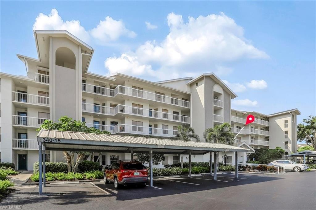 Multi-story condominium building featuring a light-toned exterior with multiple balconies and a covered parking area