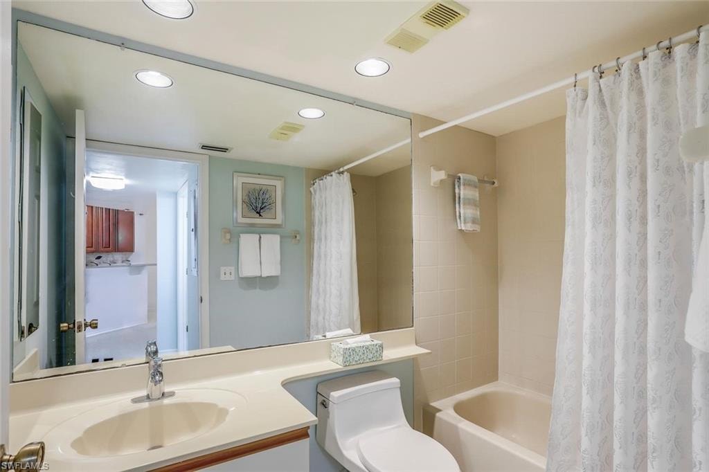 Bathroom featuring a vanity with an integrated sink, a large wall-mounted mirror, recessed lighting, and a combination tub and shower with tile surround