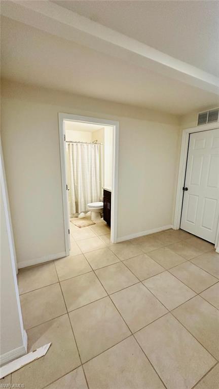 Neutral tone tile flooring extending into a full bathroom with a dark wood vanity and white toilet