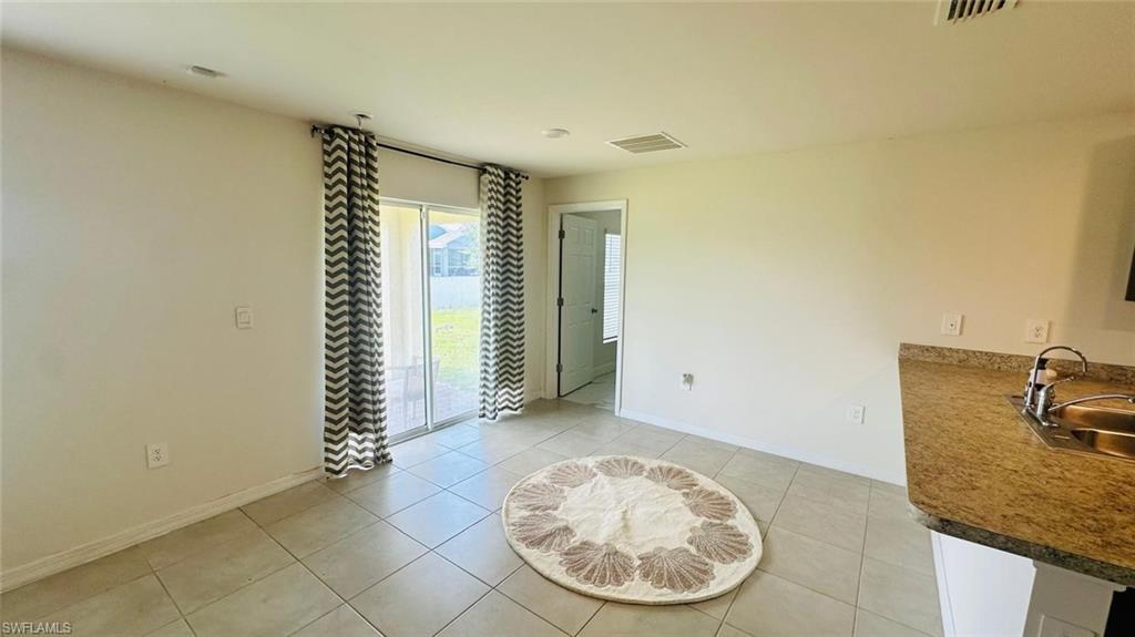 Open-concept living area featuring neutral tile flooring, a sliding glass door for outdoor access, and a kitchen counter with an undermount sink