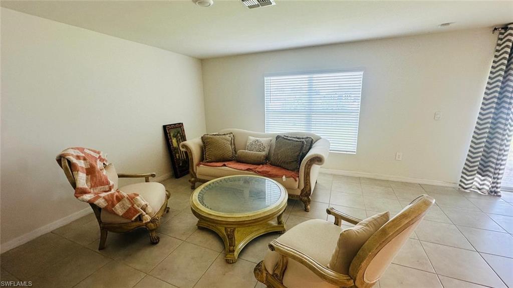 Spacious room featuring tile flooring, neutral wall tones, a large window with horizontal blinds, and a sliding glass door