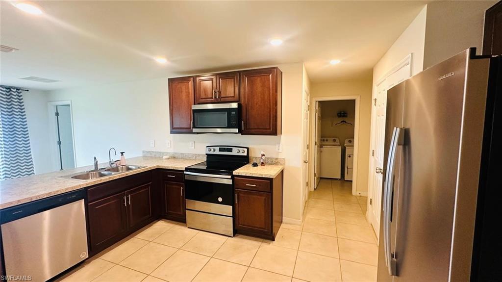 Kitchen featuring wood cabinetry, light-toned countertops, a stainless steel sink, and stainless steel appliances including a range, microwave, and dishwasher