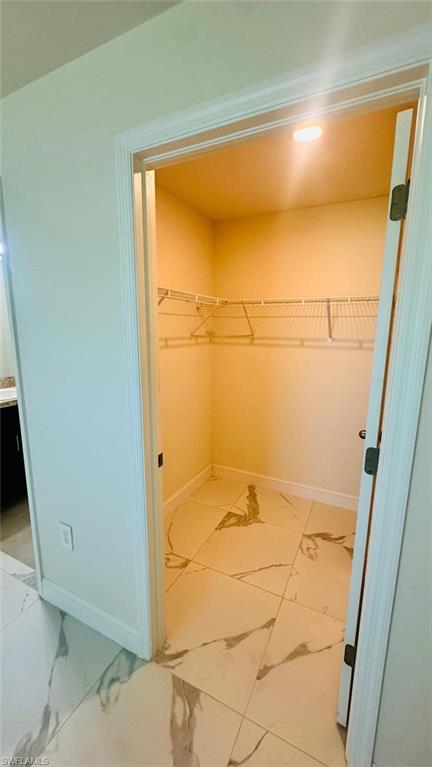 Walk-in closet featuring wire shelving, recessed lighting, and large format marbled tile flooring