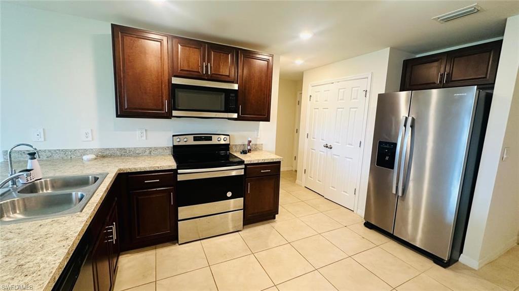Kitchen featuring abundant dark wood cabinetry, light-toned granite-style countertops, a double basin stainless steel sink, and stainless steel appliances including a built-in microwave and side-by-side refrigerator