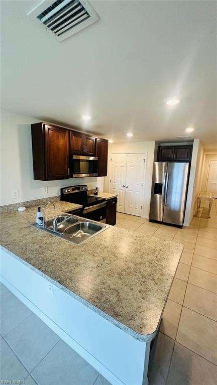 Kitchen featuring dark wood cabinetry, stainless steel appliances, a double basin sink, recessed lighting, and light-toned tile flooring