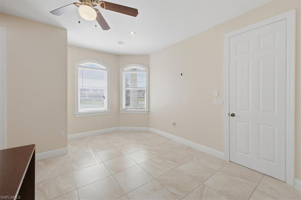 Spacious interior room featuring light-toned tile flooring, arched windows with blinds, a ceiling fan with integrated lighting, and recessed ceiling lights