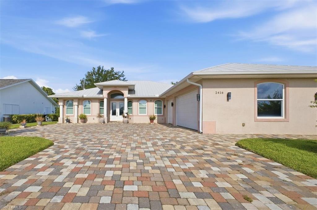 Contemporary stucco exterior featuring an arched entryway with double doors, symmetrical columns, and an integrated two-car garage