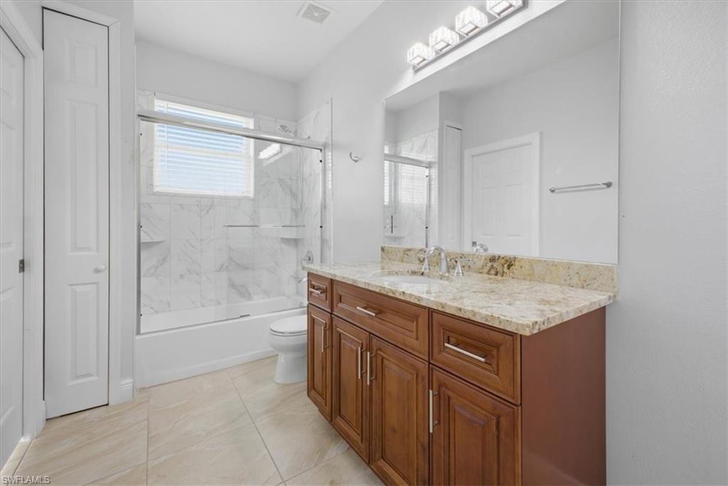 Bathroom featuring a wood-finish vanity with a light-toned countertop, a large wall-mounted mirror, and a tiled shower with clear glass enclosure