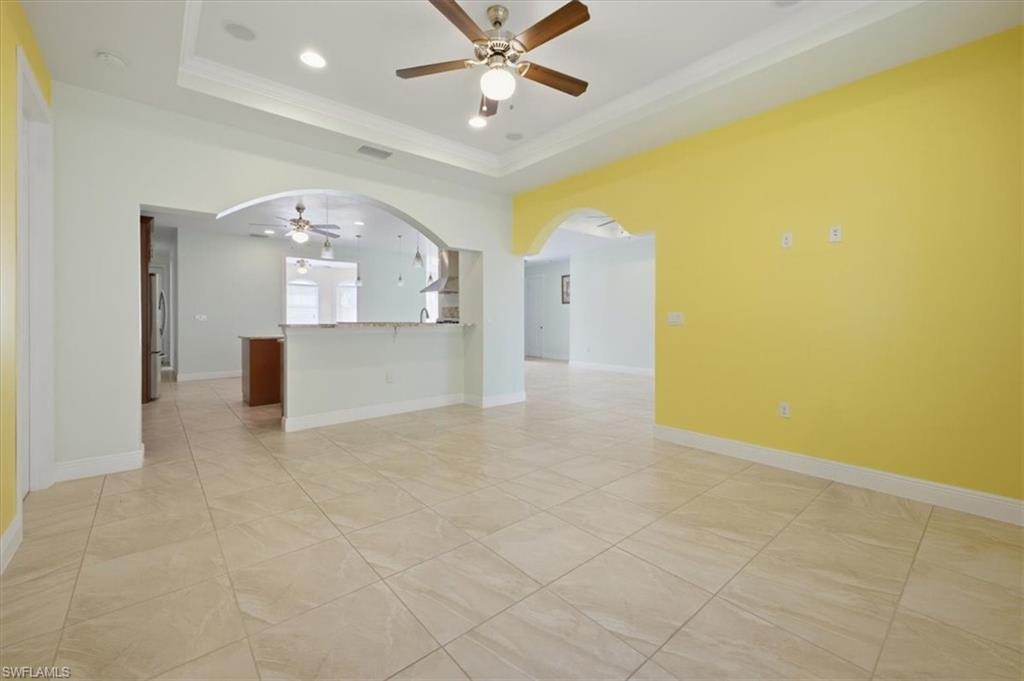 Spacious interior featuring large format tile flooring, crown molding, a tray ceiling with recessed lighting and a ceiling fan, and arched doorways