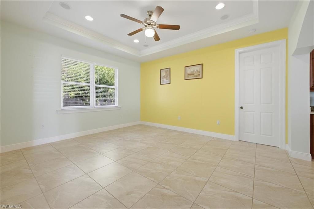 Recessed lighting, a ceiling fan, and a tray ceiling illuminate this room featuring light-toned tile flooring and a window with blinds