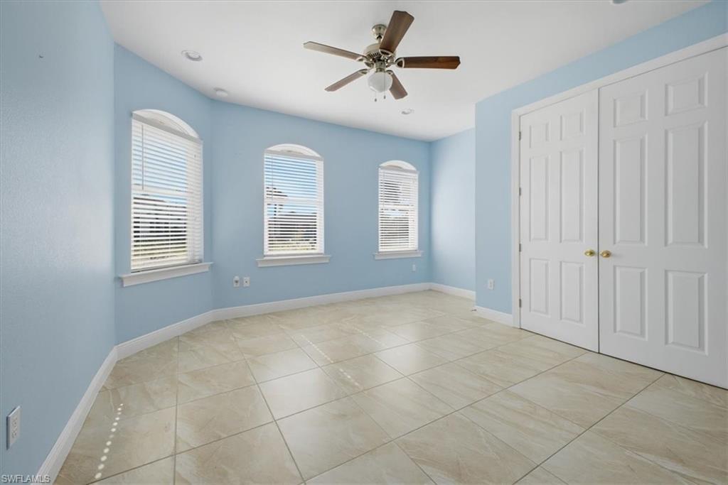 Room featuring large format floor tiles, three arched windows with blinds, a ceiling fan, recessed lighting, and double bi-fold closet doors