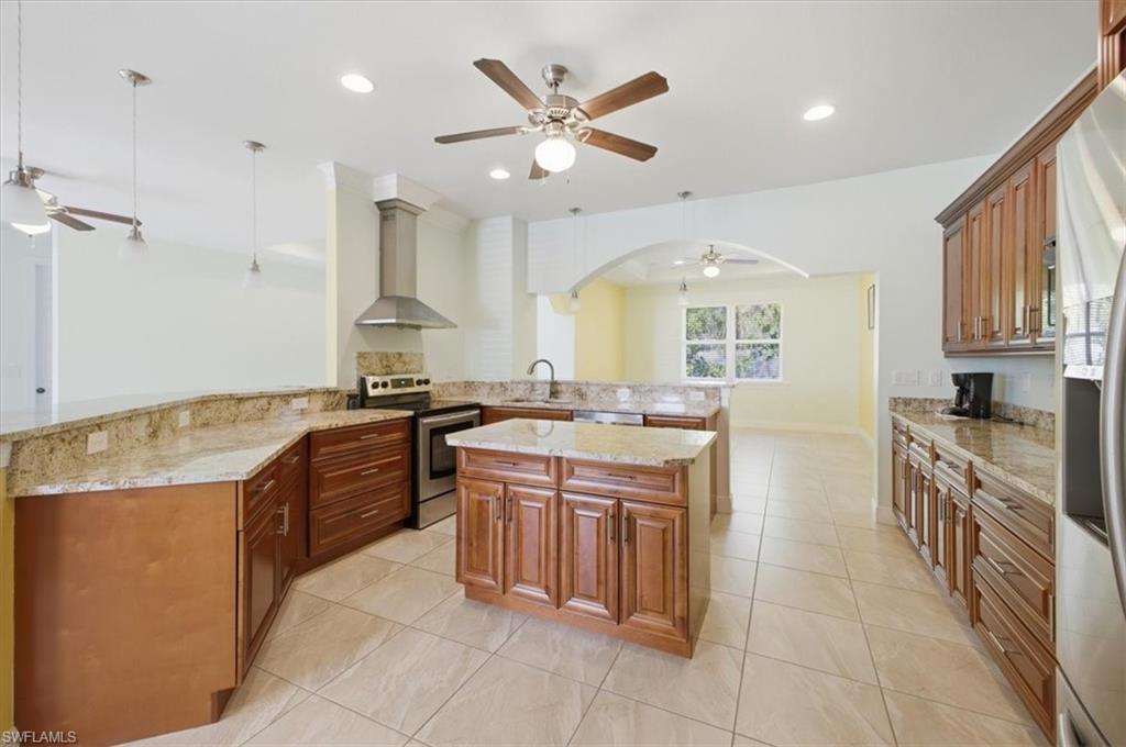 Spacious kitchen featuring warm wood cabinetry, light granite countertops, a central island, stainless steel appliances, and tile flooring