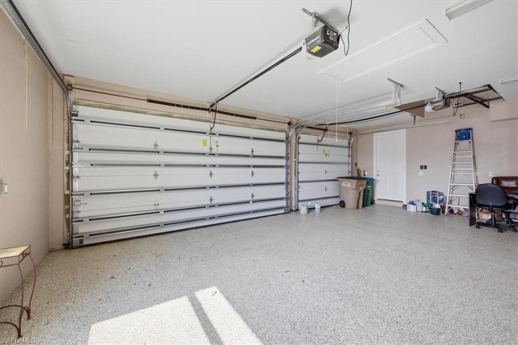 Spacious garage featuring two sectional garage doors with automatic openers, a speckled epoxy floor finish, and a side access door